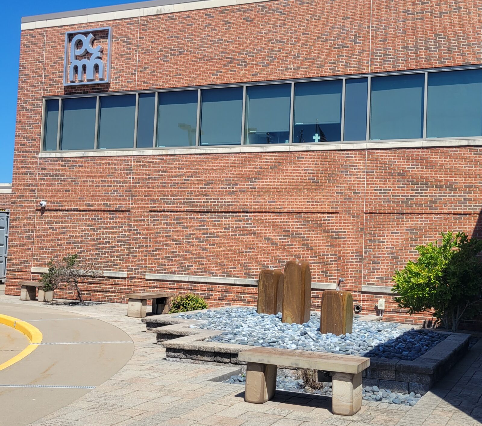 The side of a hospital building with the letters PMH near the top. A fountain structure is in front of the building.